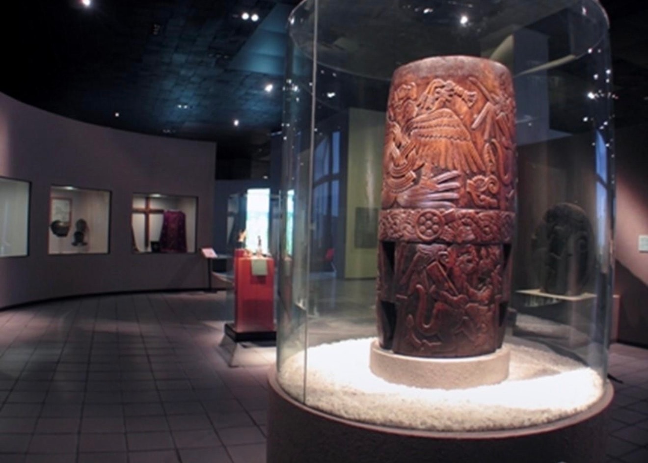 Tlalpanhuēhuētl of Malinalco on display in a museum, housed in a glass case — a large carved cylindrical drum from the Late Postclassic Mexica period